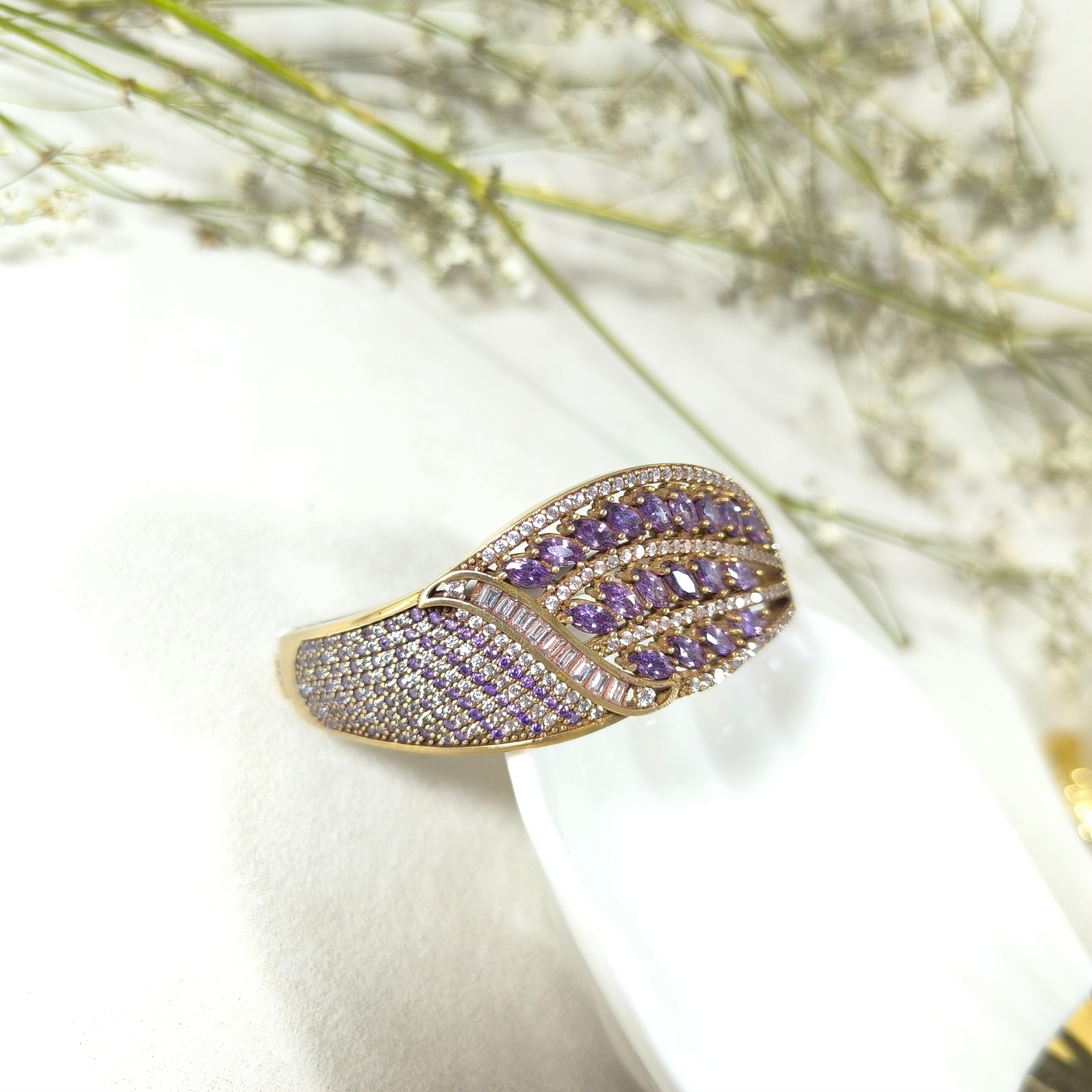 Affirmez votre élégance avec ce bracelet antique en bronze et argent, une pièce luxueuse inspirée des bijoux royaux d’autrefois. Son design richement orné de pierres violettes taillées en forme marquise, rehaussées de cristaux lumineux, crée un jeu de lumière somptueux et captivant.

La structure finement travaillée associe la chaleur du bronze antique à l’éclat raffiné de l’argent, offrant un bijou à la fois noble et intemporel. Chaque détail reflète un savoir-faire artisanal d’exception, faisant de ce bra